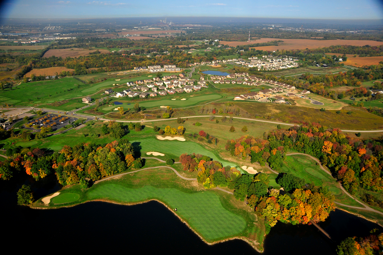 Aerial view of a golf course with autumn foliage and nearby houses.