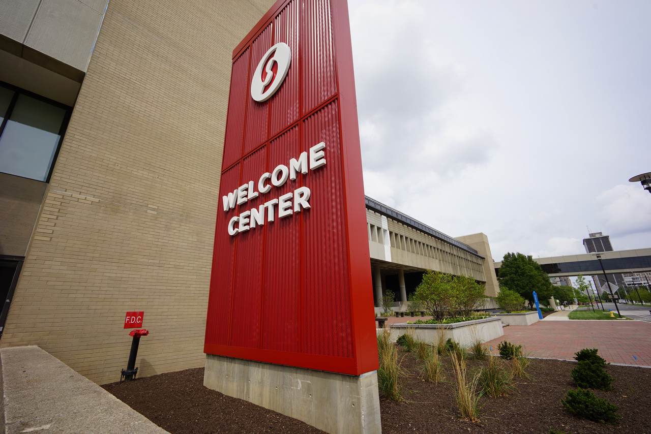 Red Welcome Center sign with white text, against a cloudy sky.