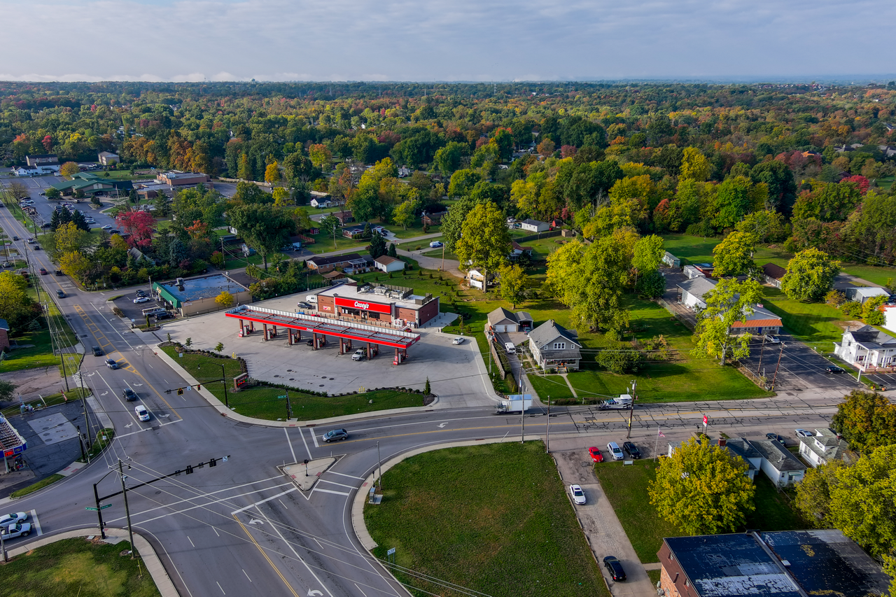 Aerial view of a gas station surrounded by trees and roads in a suburban area.