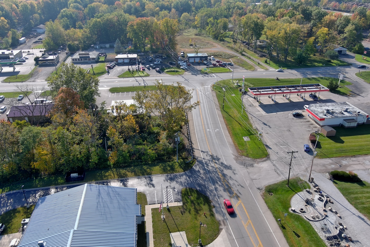 Aerial view of a tree-lined intersection with a red car and nearby buildings.