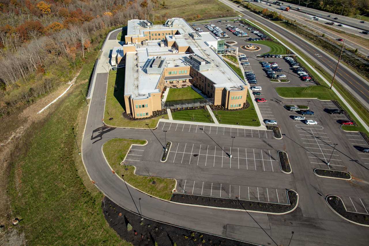 Aerial view of a modern building with parking lots and nearby road.