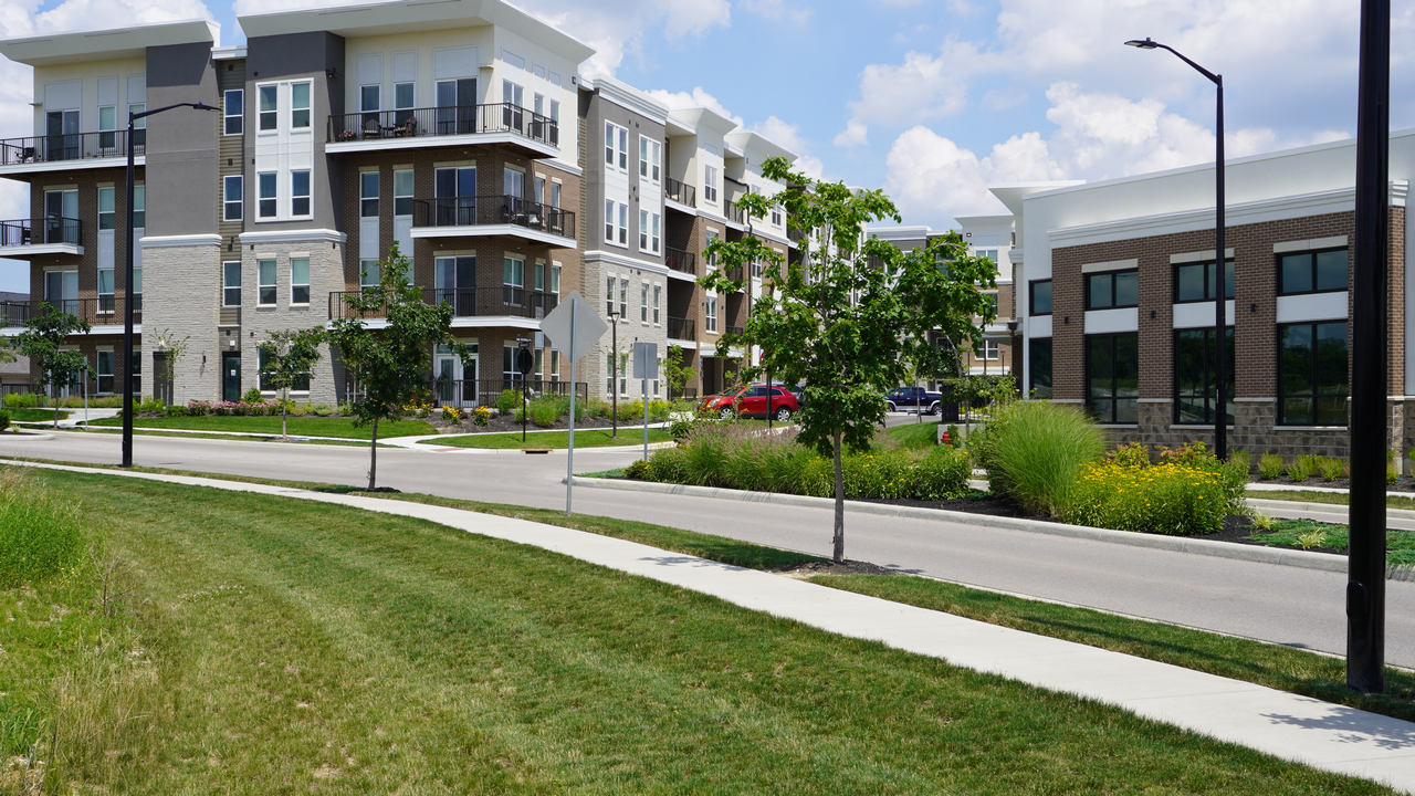 Modern apartment buildings with trees and grassy sidewalks under a clear sky.
