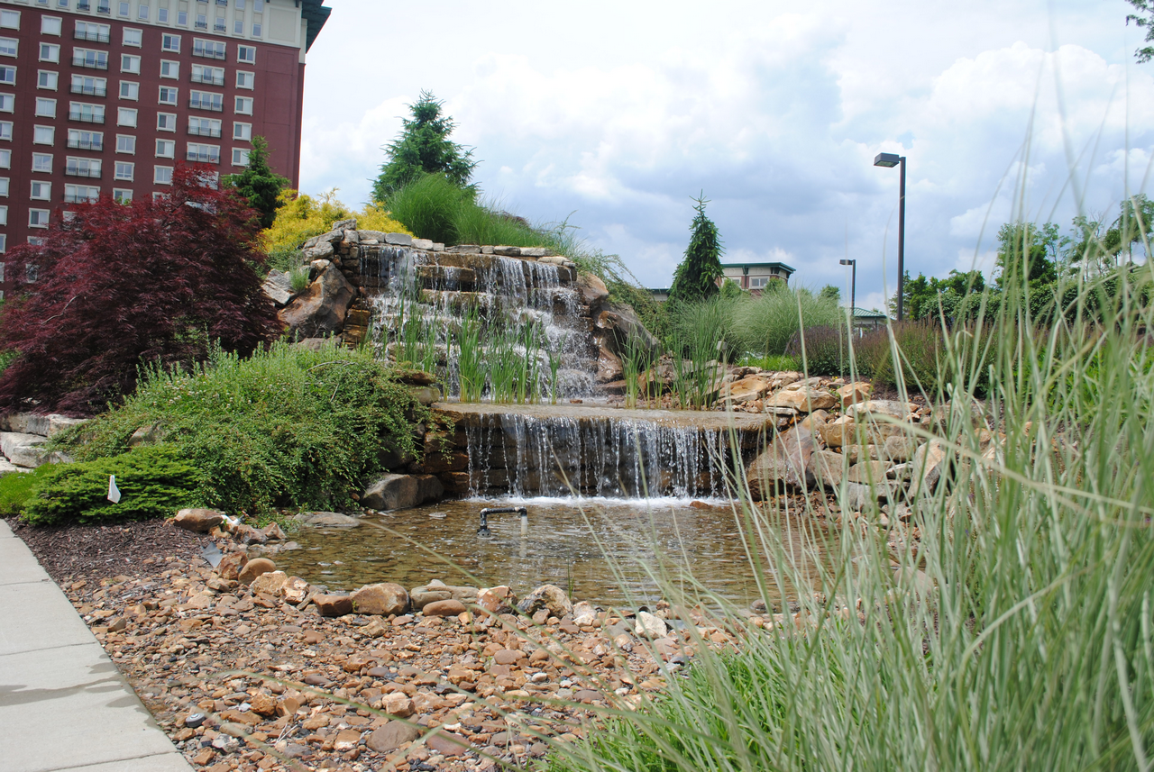 Waterfall in a landscaped garden with tall grasses and a building in the background.