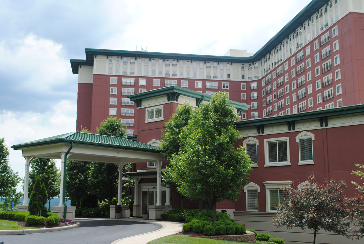Red brick hotel with green roof accents and lush landscaping.