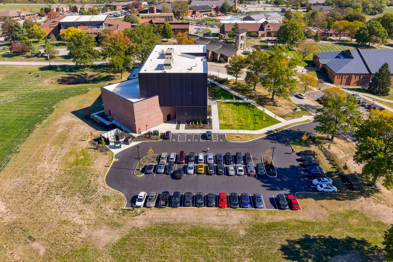 Aerial view of a building with a parking lot and surrounding greenery.