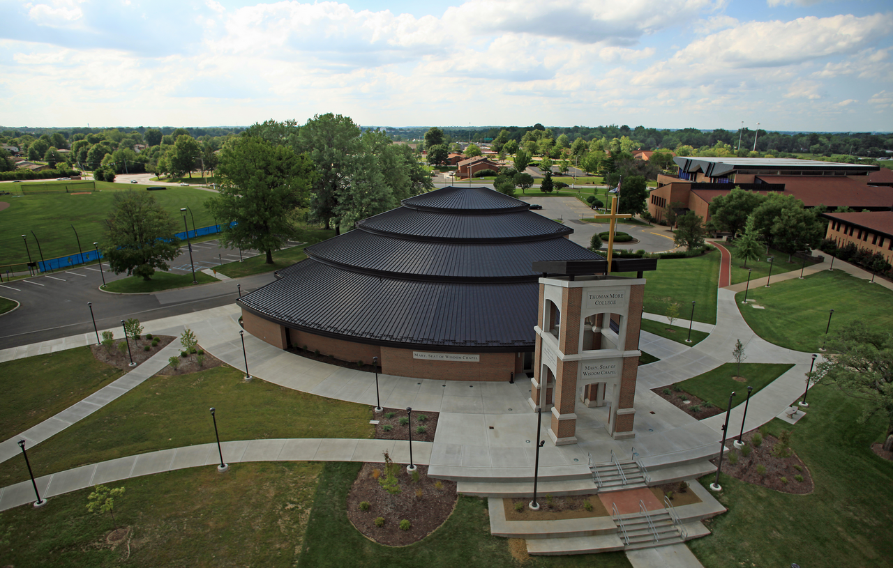 Circular building with tiered roof near a clock tower, surrounded by green lawns.