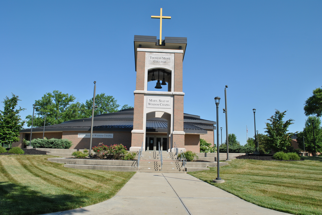Church with a large cross and clock tower, surrounded by greenery under a clear blue sky.