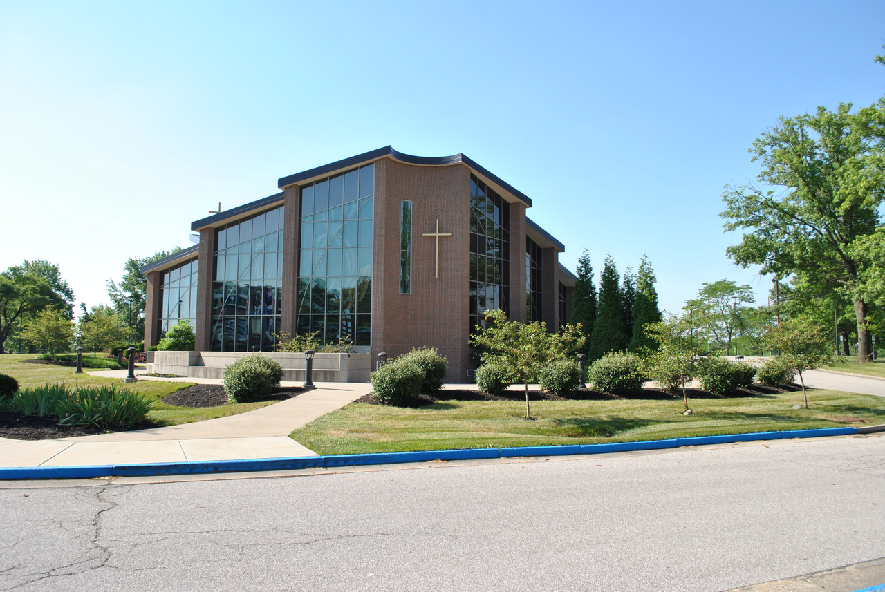 Large brick church with glass windows, surrounded by greenery, under a clear blue sky.