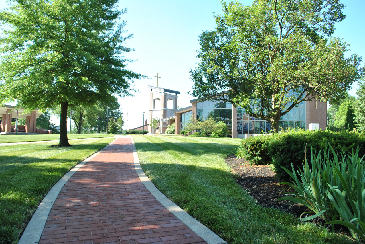 Red brick path through a green campus with trees and buildings.