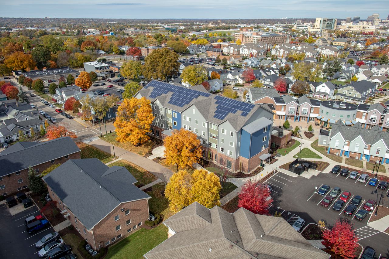 Aerial view of suburban neighborhood in autumn with colorful trees and solar panels on roofs.