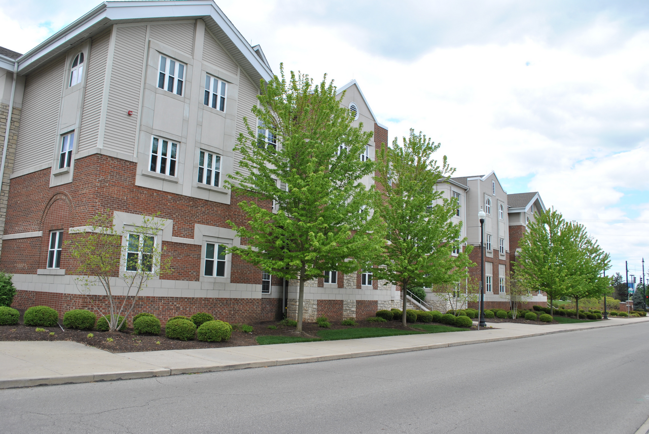 Brick building with trees along a quiet street under a cloudy sky.