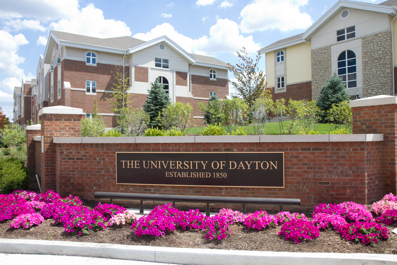 University of Dayton entrance sign with pink flowers and brick buildings.