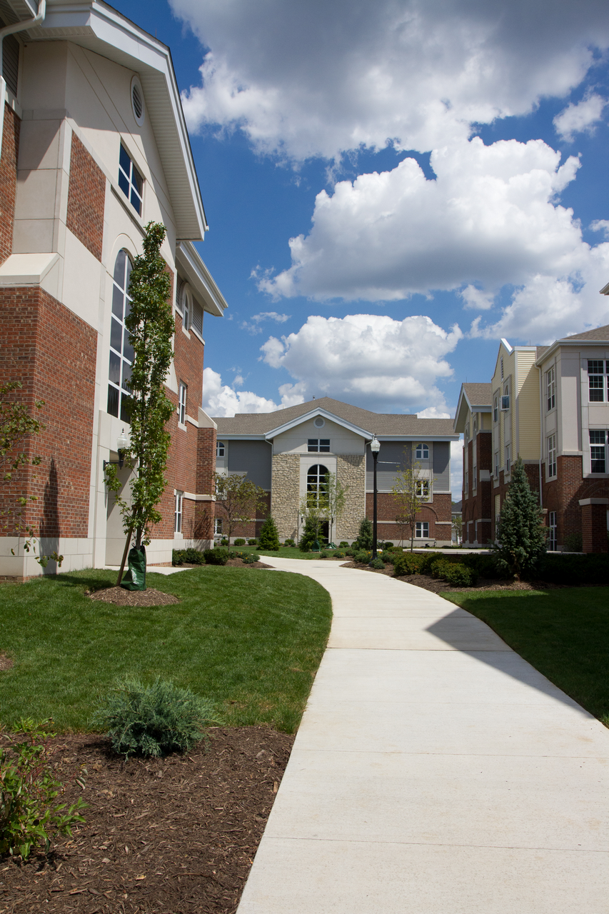 Campus walkway lined with brick buildings, under a partly cloudy sky.