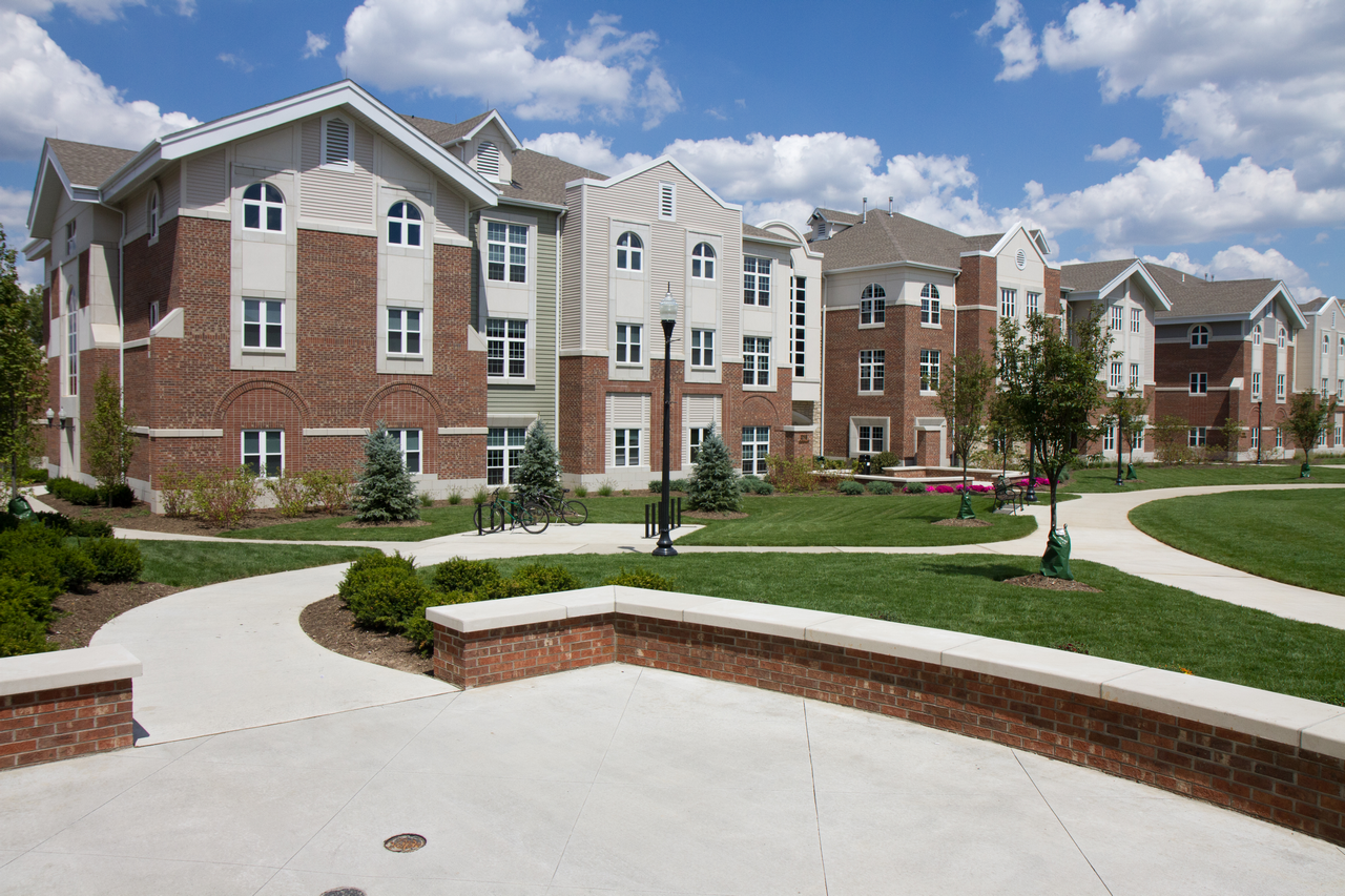 Large brick college buildings with green lawns and pathways under a blue sky.