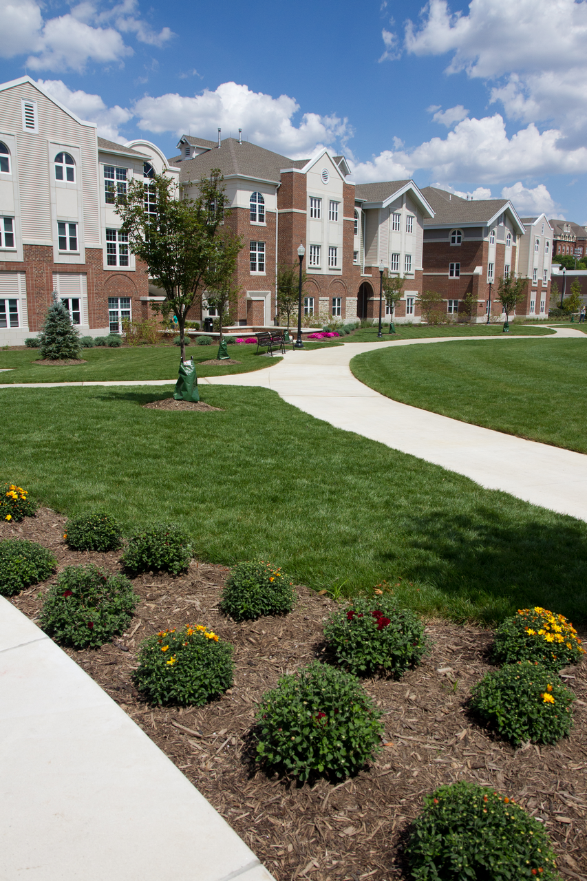 Campus lawn with curved walkway, brick buildings, and blue sky.