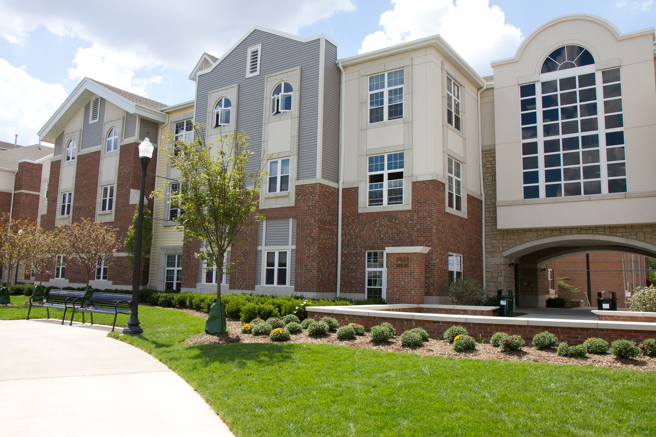 Campus building with arched window, trees, and walkway on a sunny day.
