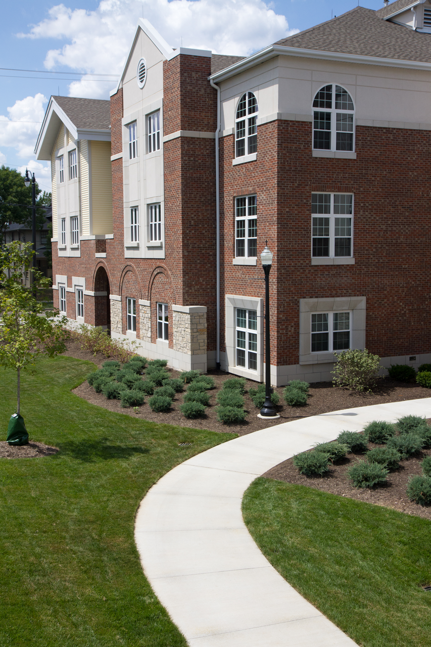 Brick building with arched windows, sidewalk, and landscaped shrubs.