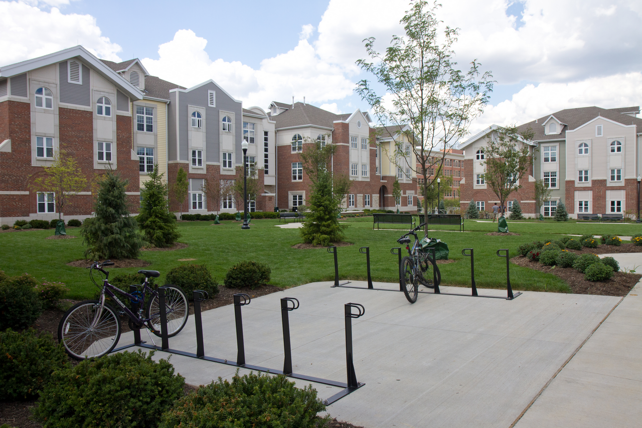 Bicycles parked near modern red-brick apartments under a partly cloudy sky.