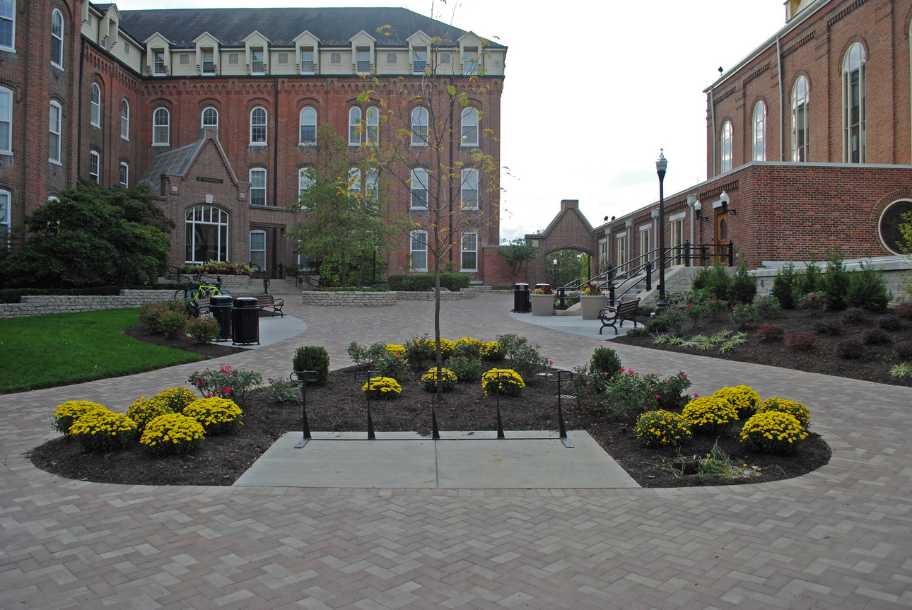 Brick courtyard with yellow flowers, trees, and historic buildings.