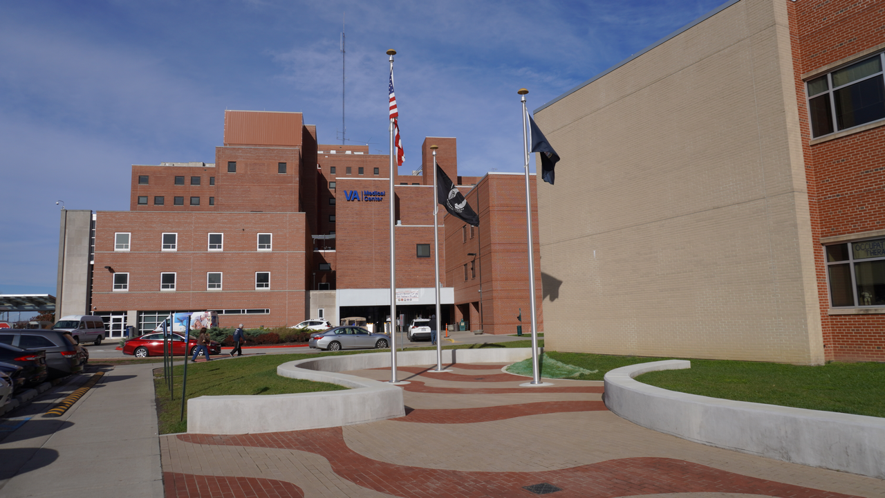 Hospital entrance with three flagpoles and a brick pathway.