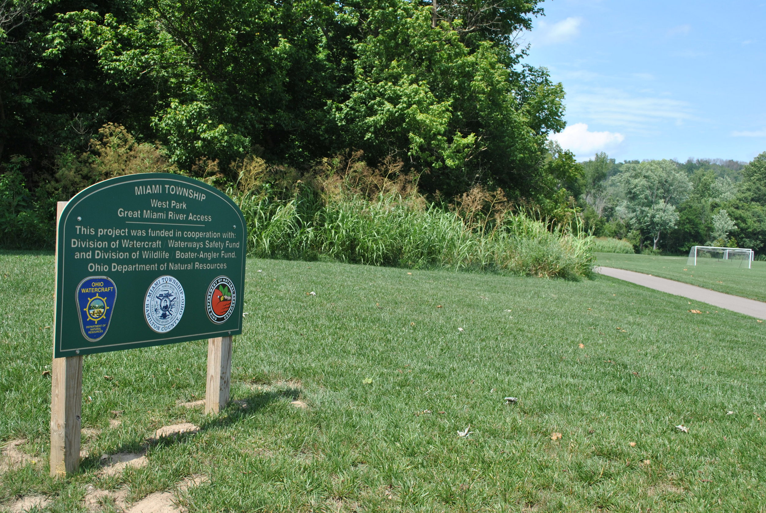 Park sign on grassy area with path and trees in background.