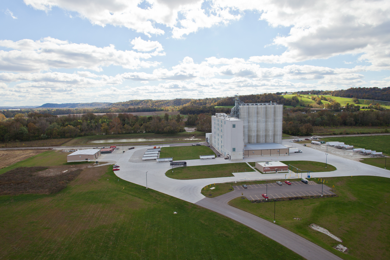 Large industrial building on a grassy landscape under a cloudy blue sky.