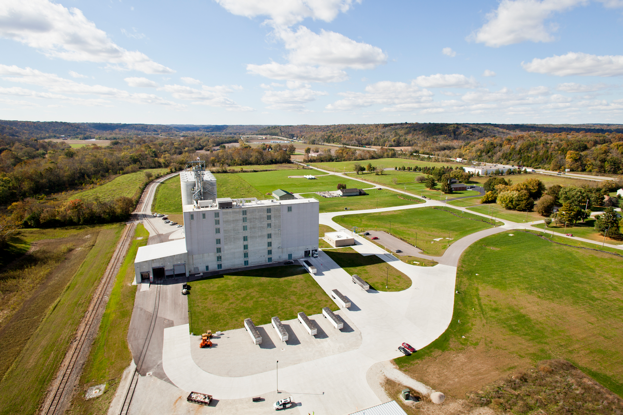 Aerial view of a large white industrial building amidst green fields.