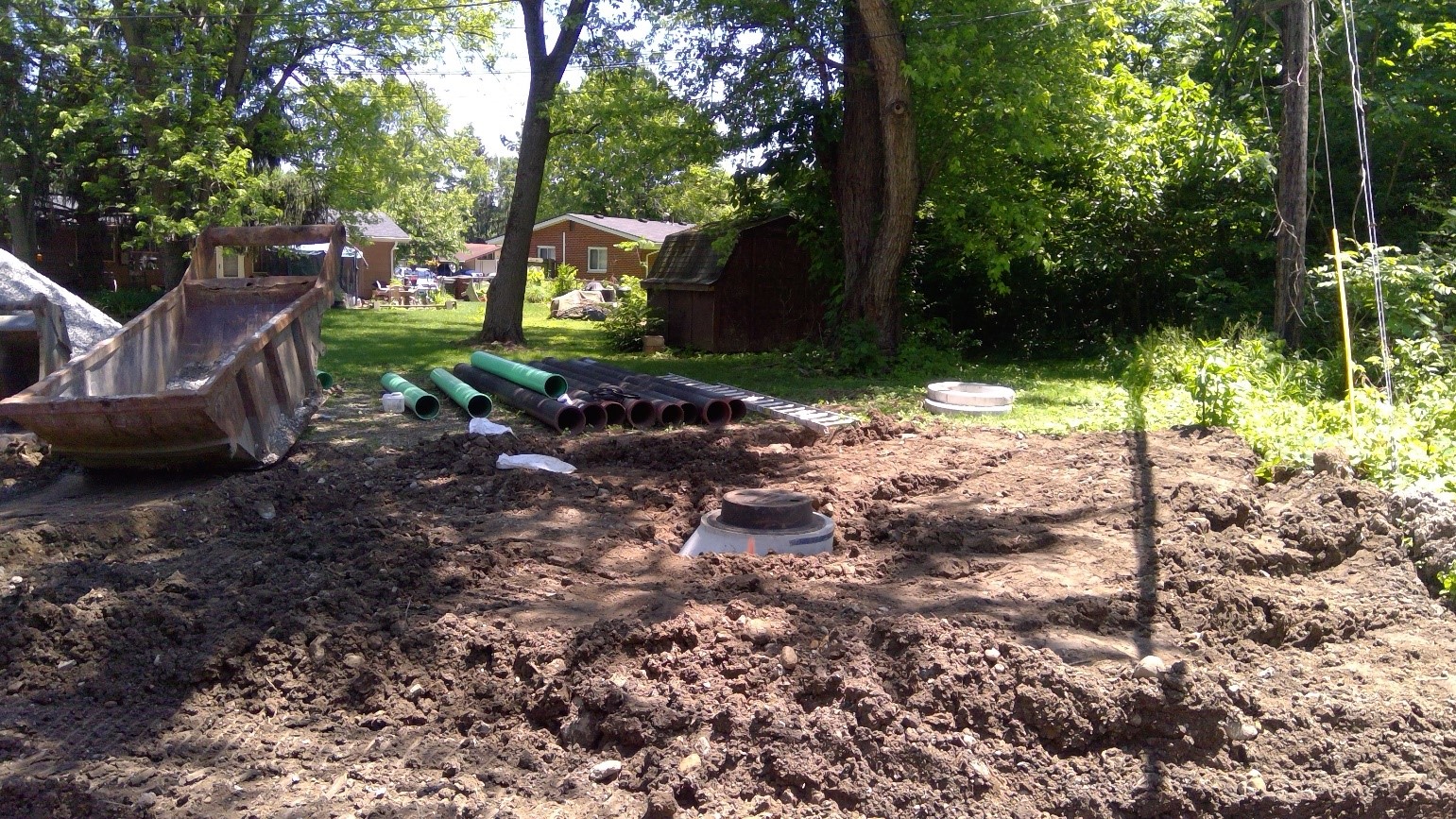 Dug-up backyard with scattered pipes and dirt under trees.
