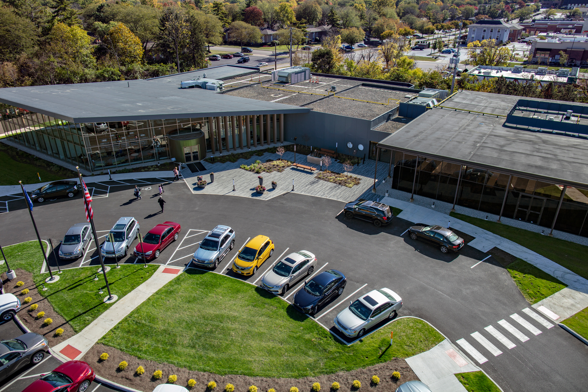 Aerial view of a modern building with parked cars and surrounding greenery.