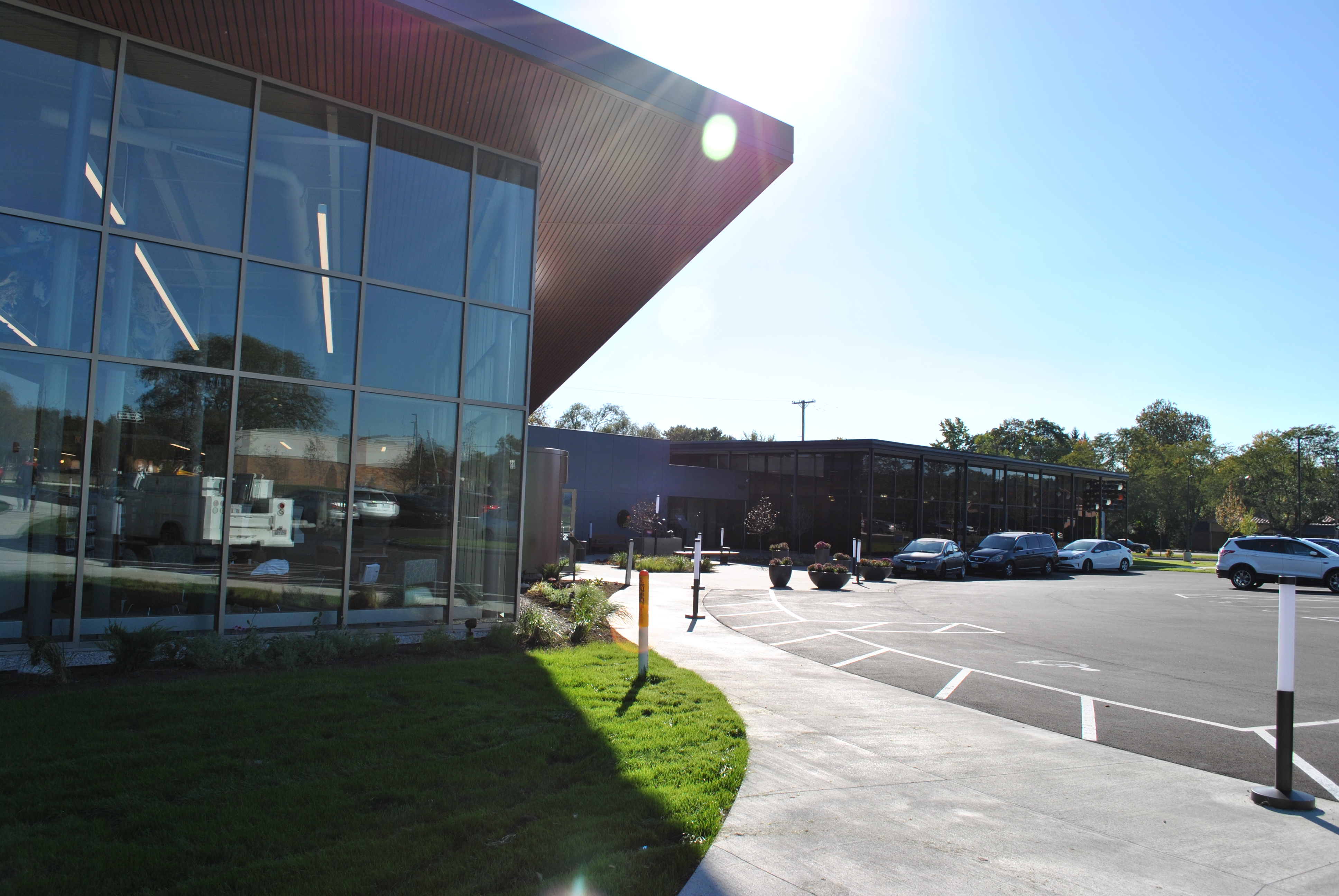 Modern building with glass facade and parking lot on a sunny day.
