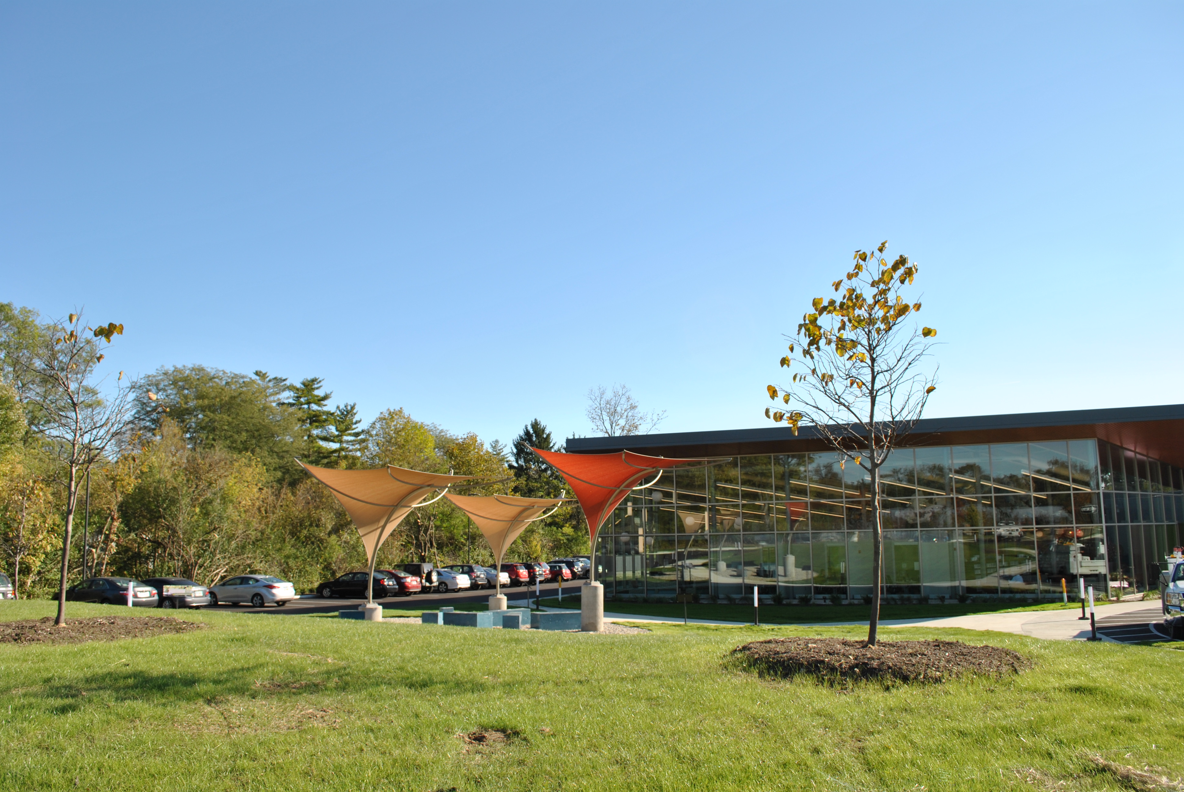 Modern building with glass facade, surrounded by green lawn and trees under clear blue sky.
