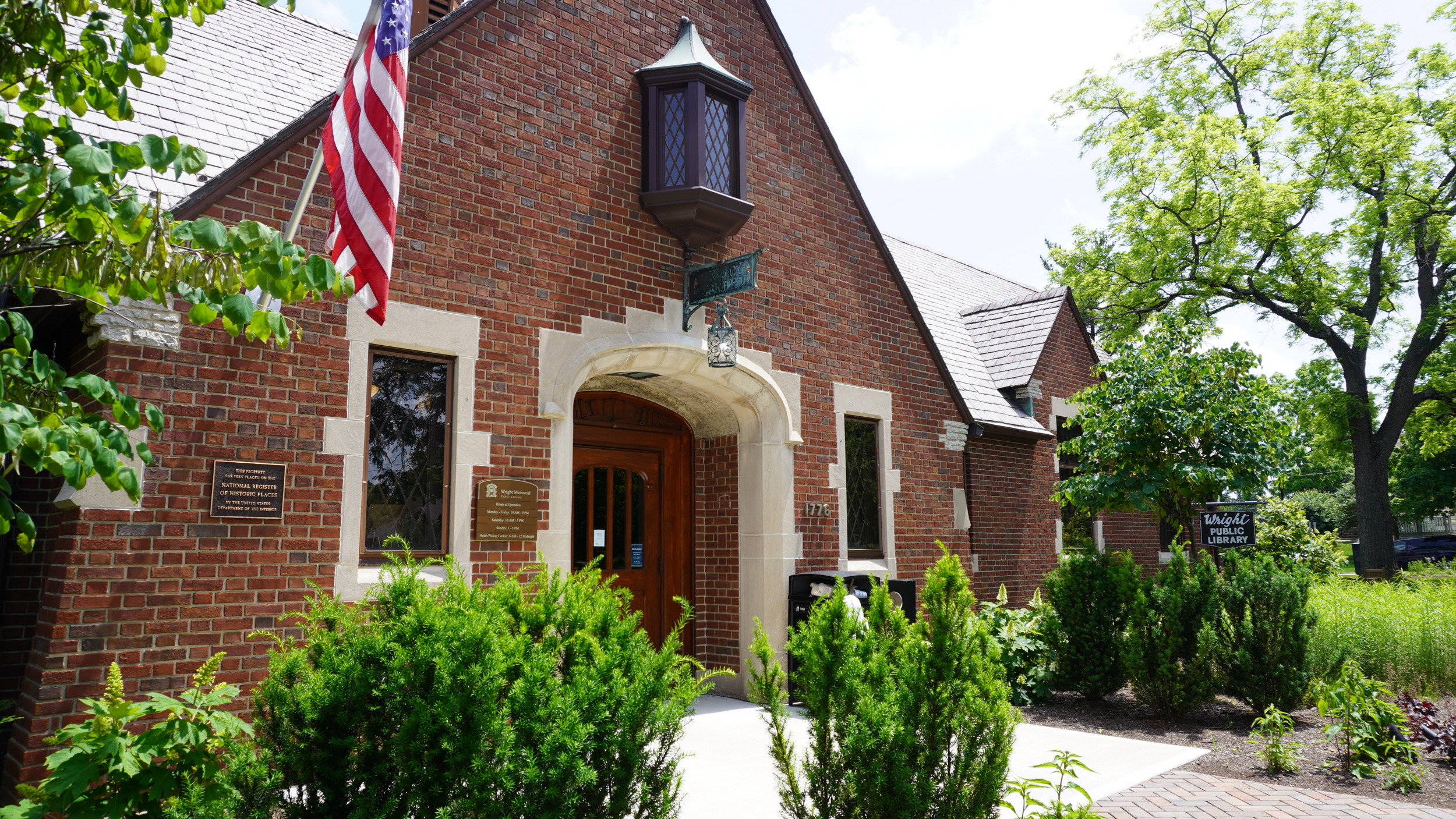 Brick building exterior with arched entrance, flag, and greenery.