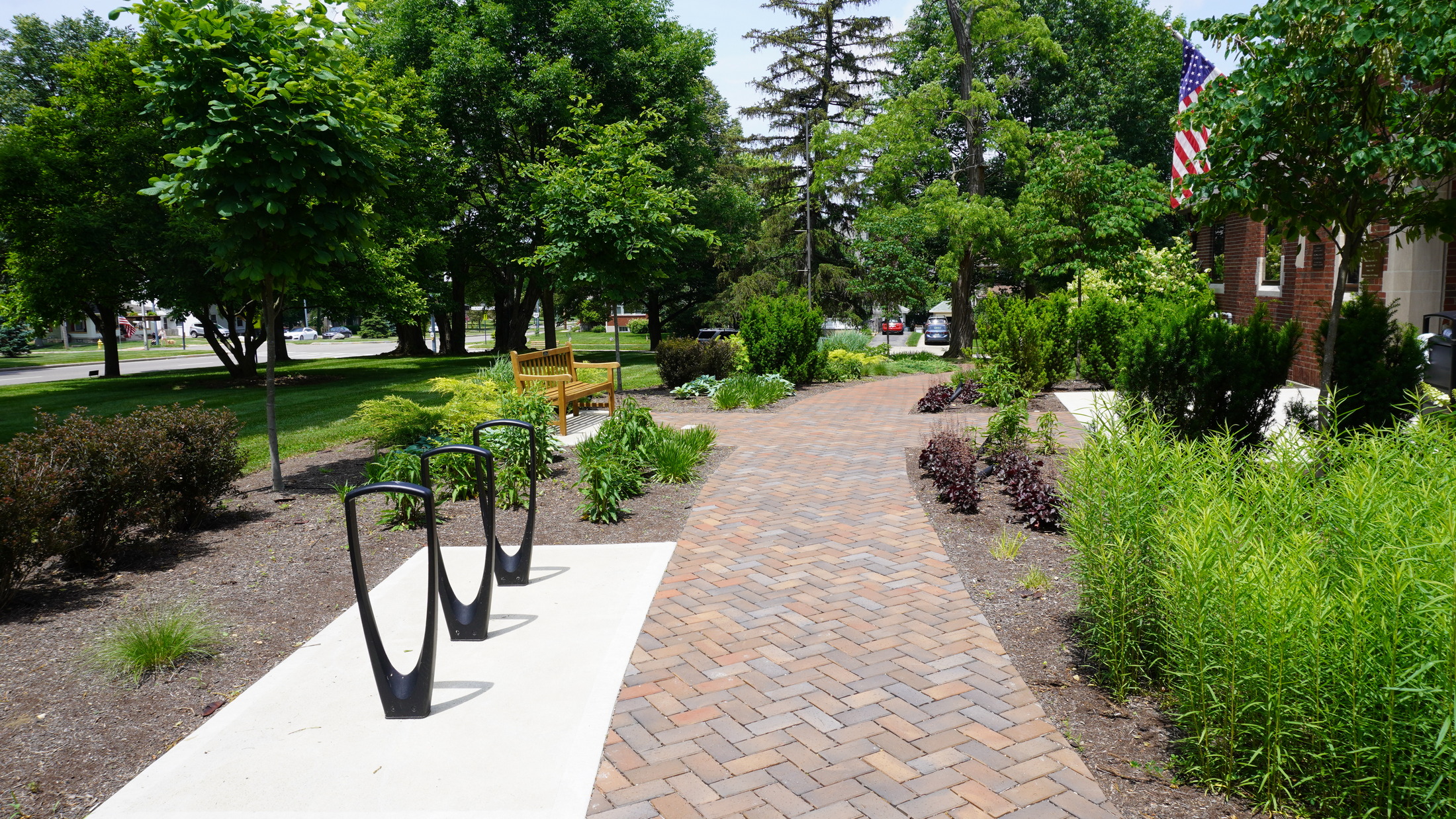 Brick pathway in a park, surrounded by green trees and bushes.