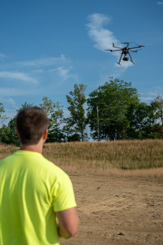 Man in yellow shirt flying a drone outdoors.