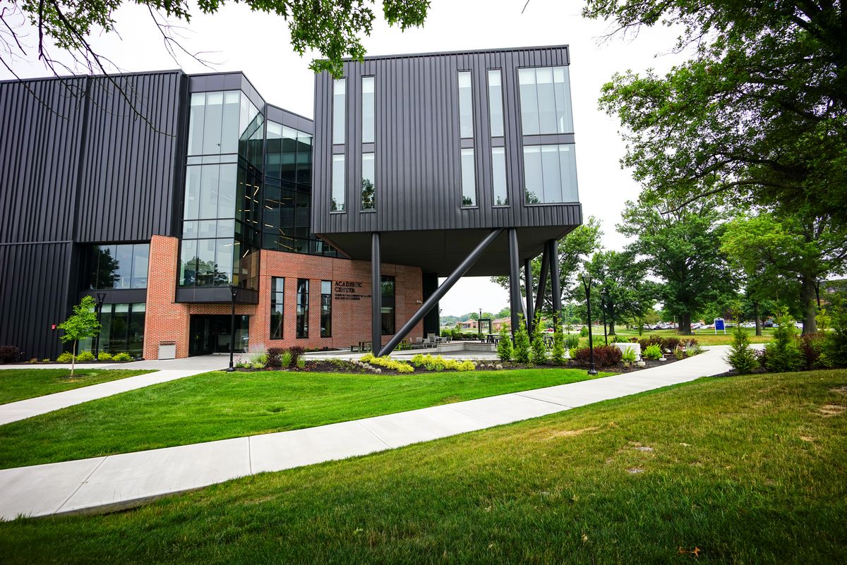 Modern building with black and brick facade, lush green lawn, and trees.