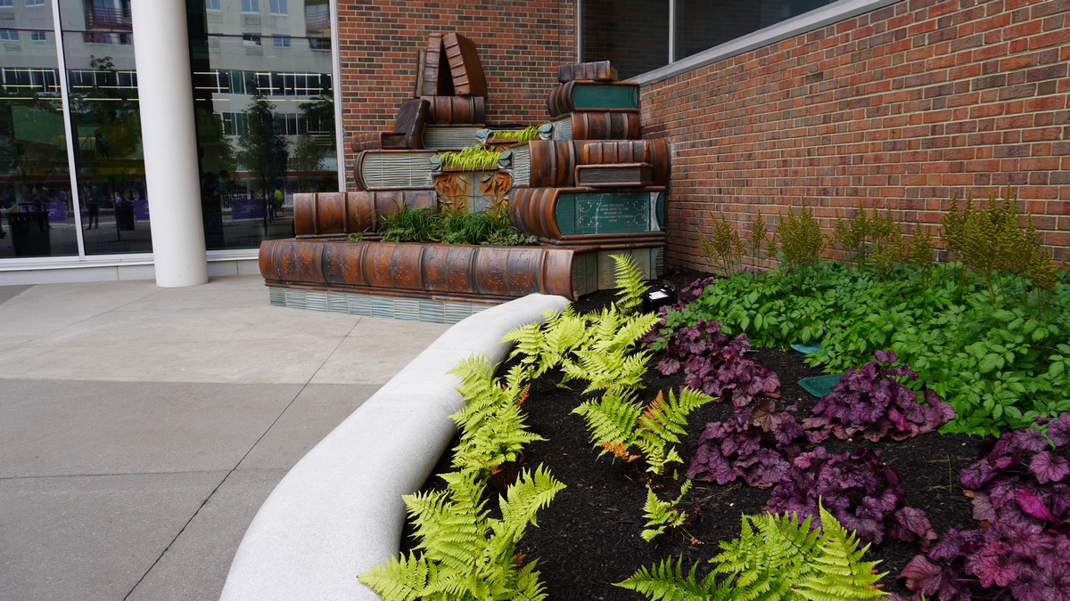Urban garden with colorful plants and stacked pipe sculpture.