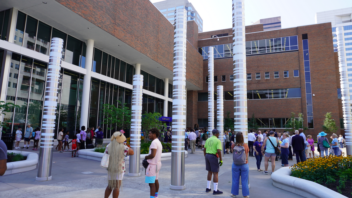 Crowd outside modern building with tall columns and lush planters.