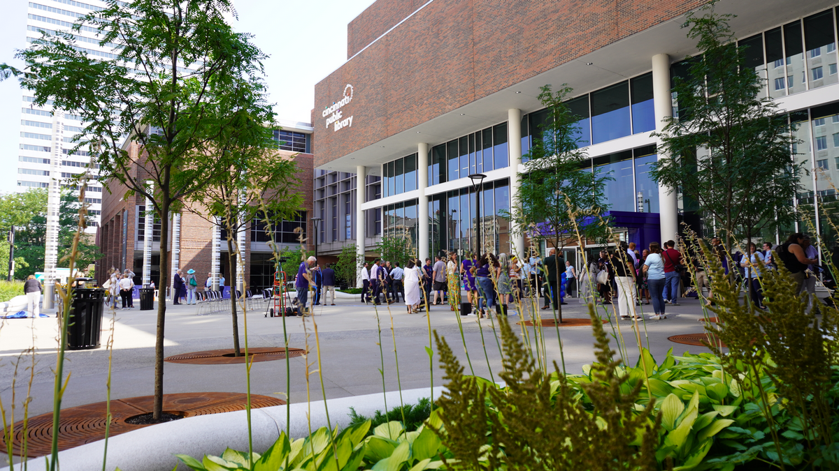 Crowd outside modern building with trees and plants in the foreground.