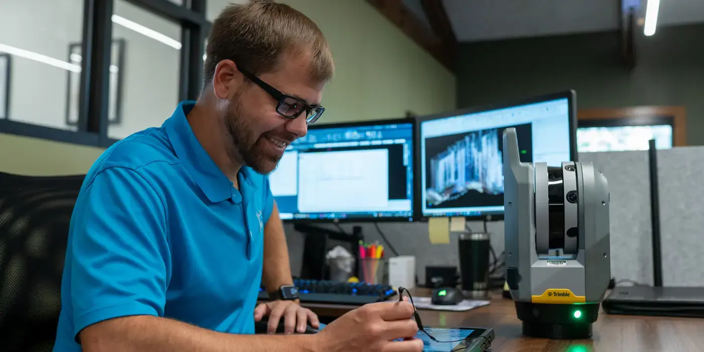 Man in a blue shirt works at a desk with dual monitors.