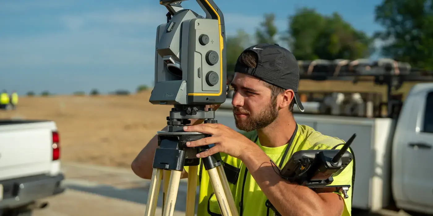 Surveyor using a theodolite on a sunny construction site.