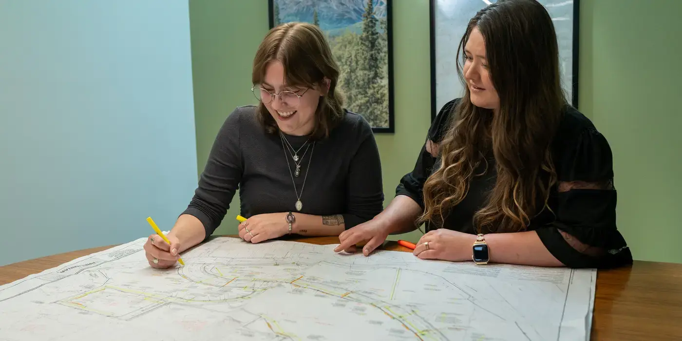 Two women smiling and marking a large map on a table.