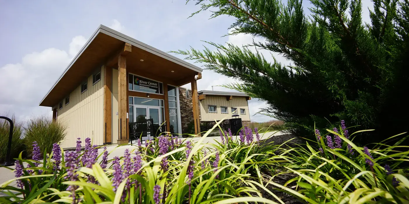 Modern building with a sloped roof, foreground of purple flowers and green shrubs.