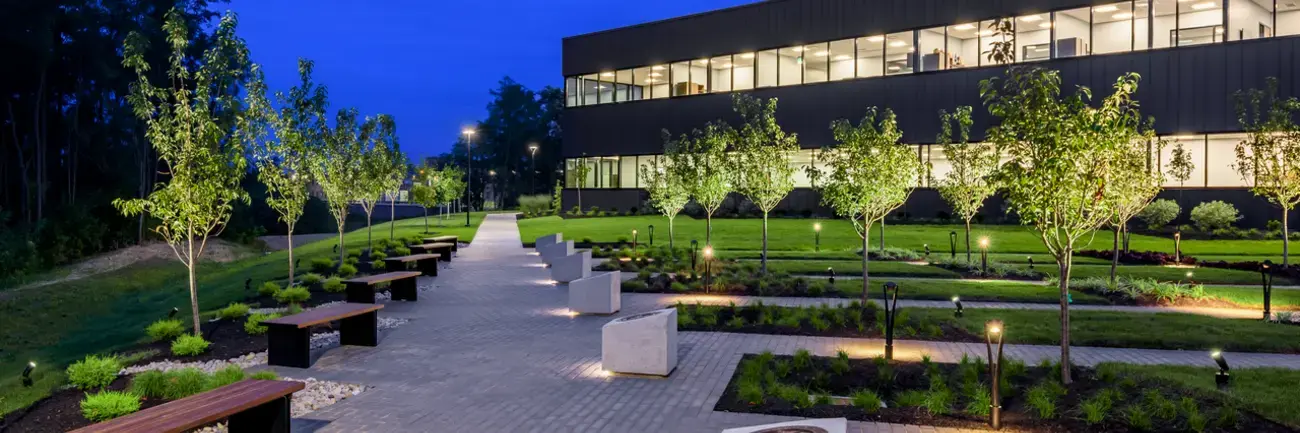 Walkway and garden beside a lit modern building at dusk.