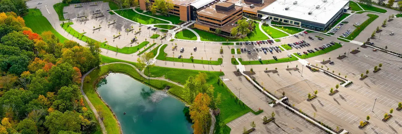 Aerial view of a campus with buildings, parking lot, and a small pond surrounded by trees.