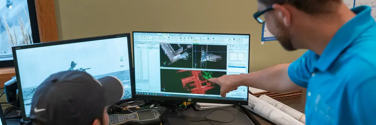 Two men working at a desk with dual computer monitors.