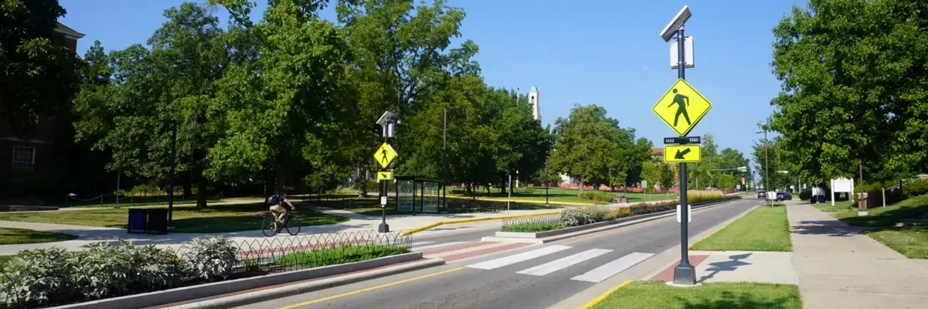 Miami University Gateways - Oxford, OH Sunny road with crosswalk, trees, and street signs on a clear day.